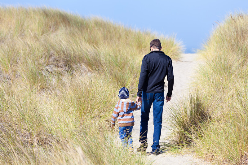 Father and son walking over sandy beach path on grassy Bandon dune.