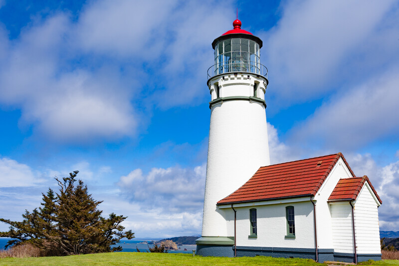 Freshly painted white lighthouse tower with red top and building on a bright sunny day.