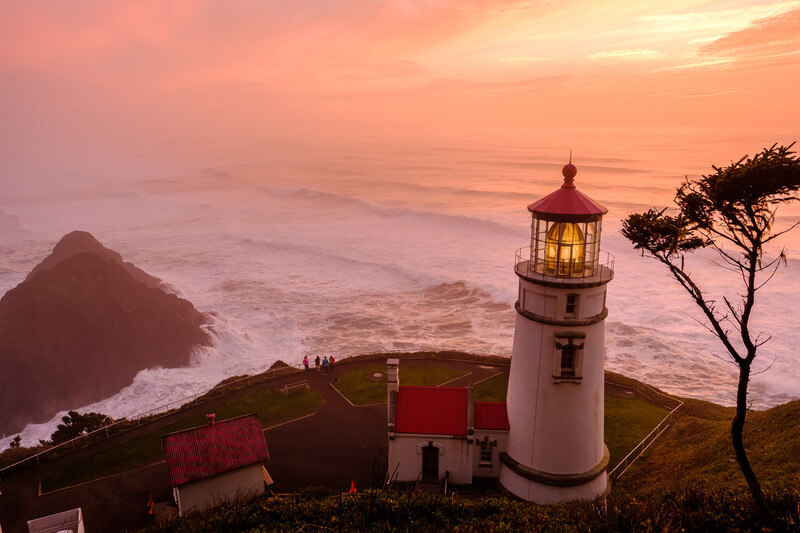 Lighthouse on a cliff at sunset overlooking the surf and a peach colored sky.