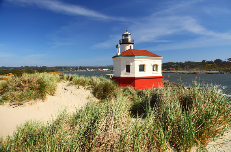 Coquille River Lighthouse, low grassy dune, and river on a sunny day.