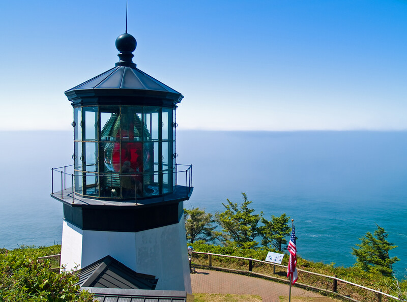 Top of the lighthouse with red fresnel lens overlooking the blue pacific and viewing area.