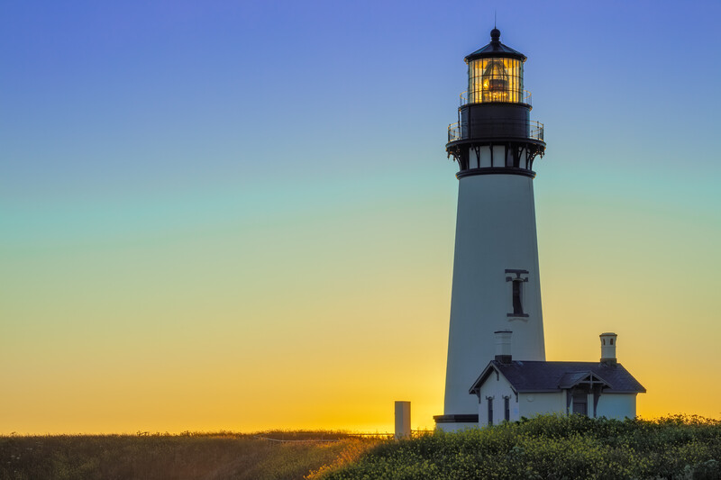 Glowing lighthouse at sunset with a blue, yellow, and orange sky.