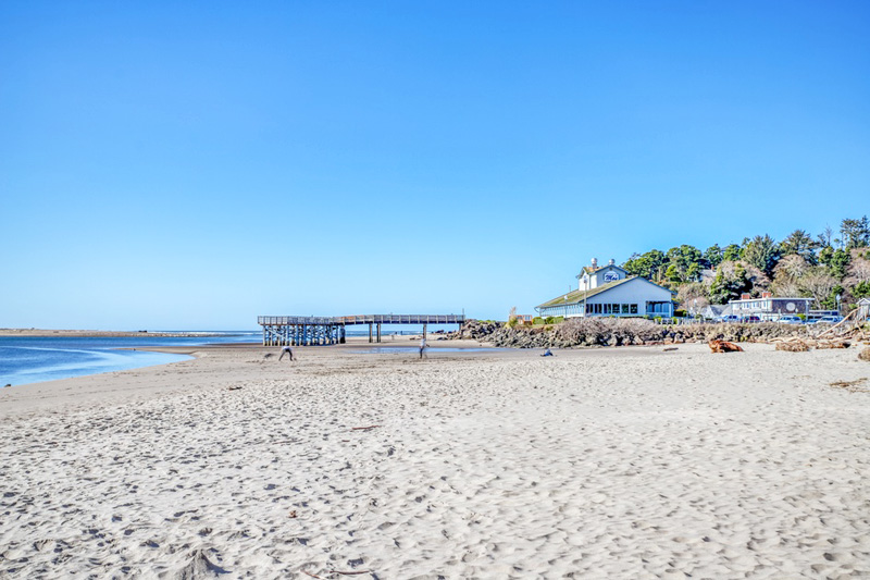 Sandy beach with fishing dock and bayfront restaurant on a sunny day.