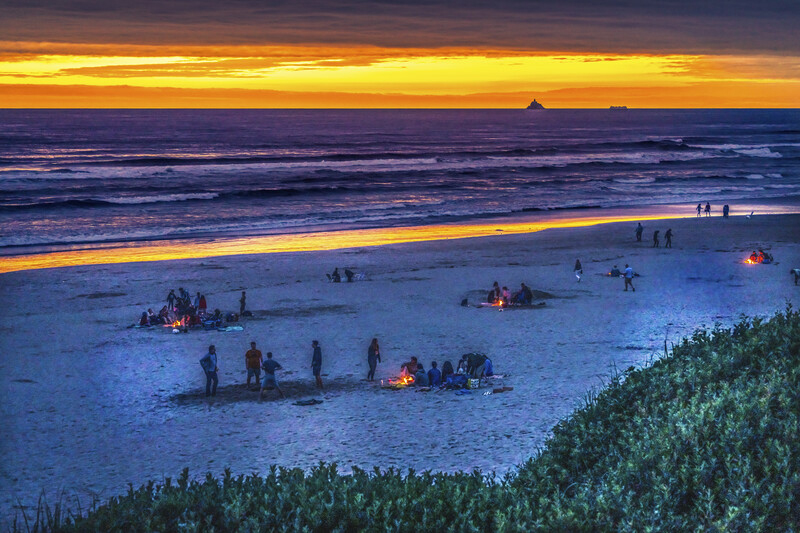 Several bonfires with friends and families glowing on the beach during a beautiful sunset.
