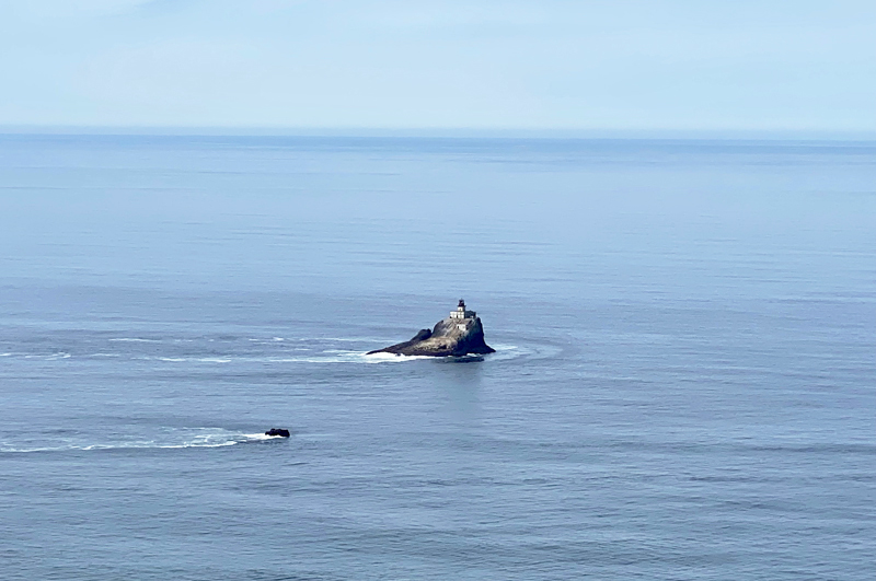 Distant view of Tillamook Rock Lighthouse (Terrible Tilly), calm Pacific Ocean, and blue sky.