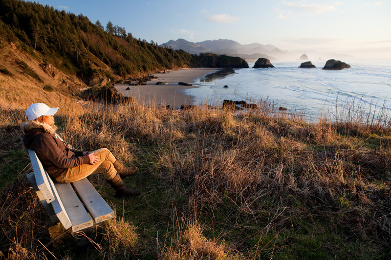 Woman sitting on a bench overlooking Ecola State Park at sunset.
