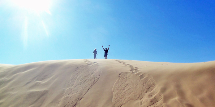 Huge sand dune with two people a the top having fun in the sun.